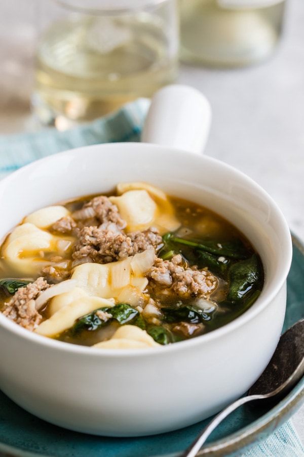 A bowl of sausage tortellini soup with spinach in it.