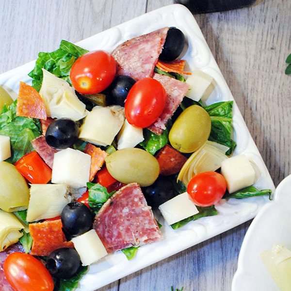 Angled view of antipasti salad on a square white plate.