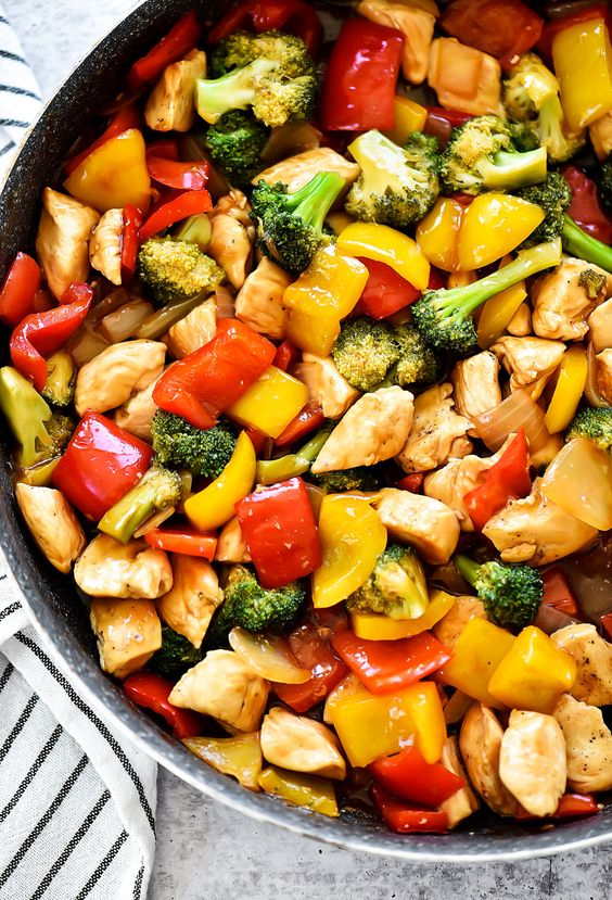 A skillet full of chicken, and diced vegetables covered in a savory sauce.