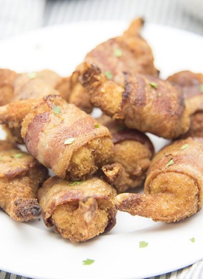 Angled view of bacon wrapped butterfly shrimp on a white plate.