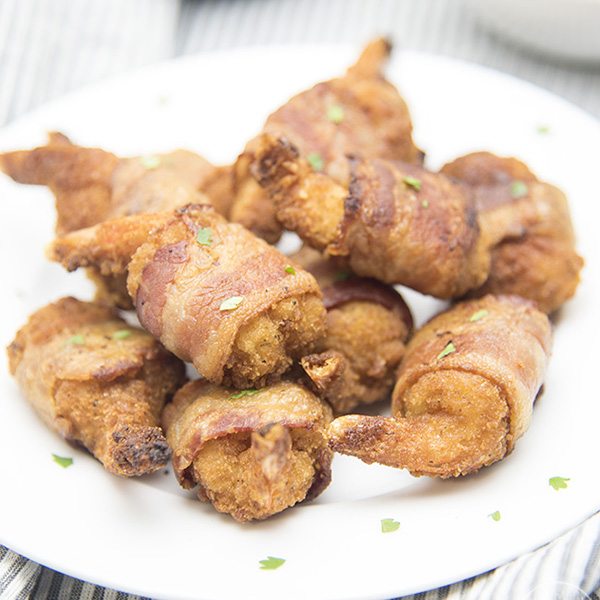 Angled view of bacon wrapped butterfly shrimp on a white plate.