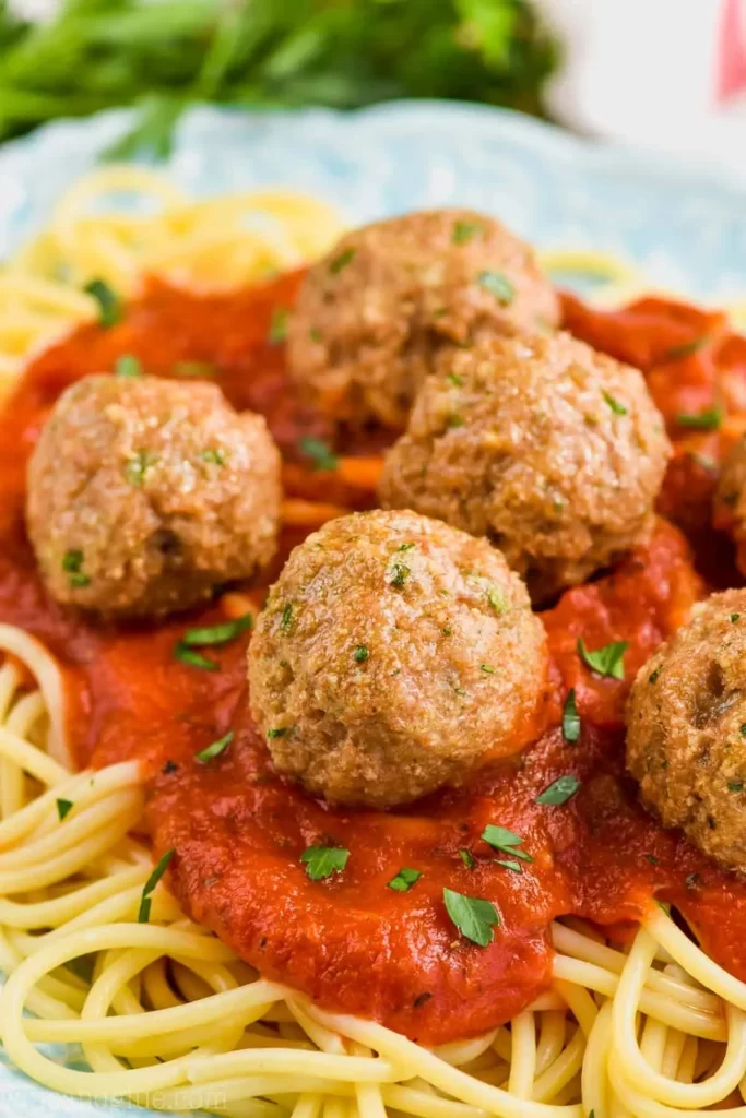 A plate of spaghetti topped with marinara sauce and homemade meatballs. 