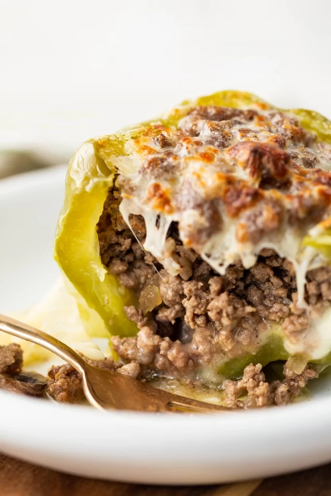A stuffed bell pepper cut open on a plate and full of ground beef, and topped with melted cheese.