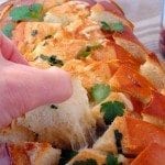 Close up image of a piece of cheesy garlic bread being pulled.