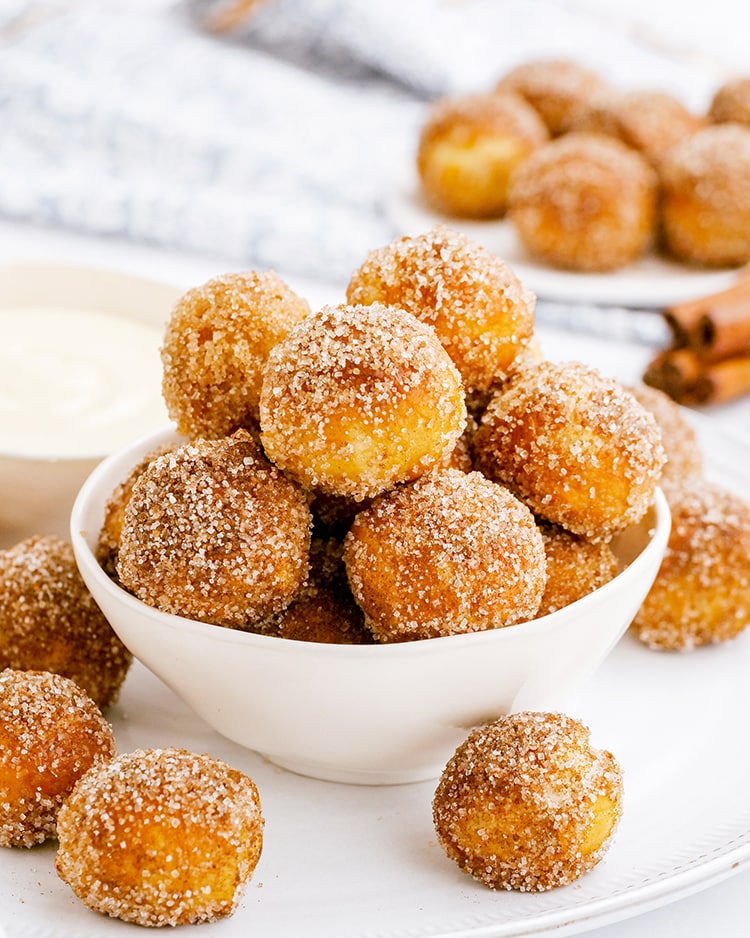 A bowl of cinnamon sugar soft pretzel bites, piled up with a few on the side of the bowl.