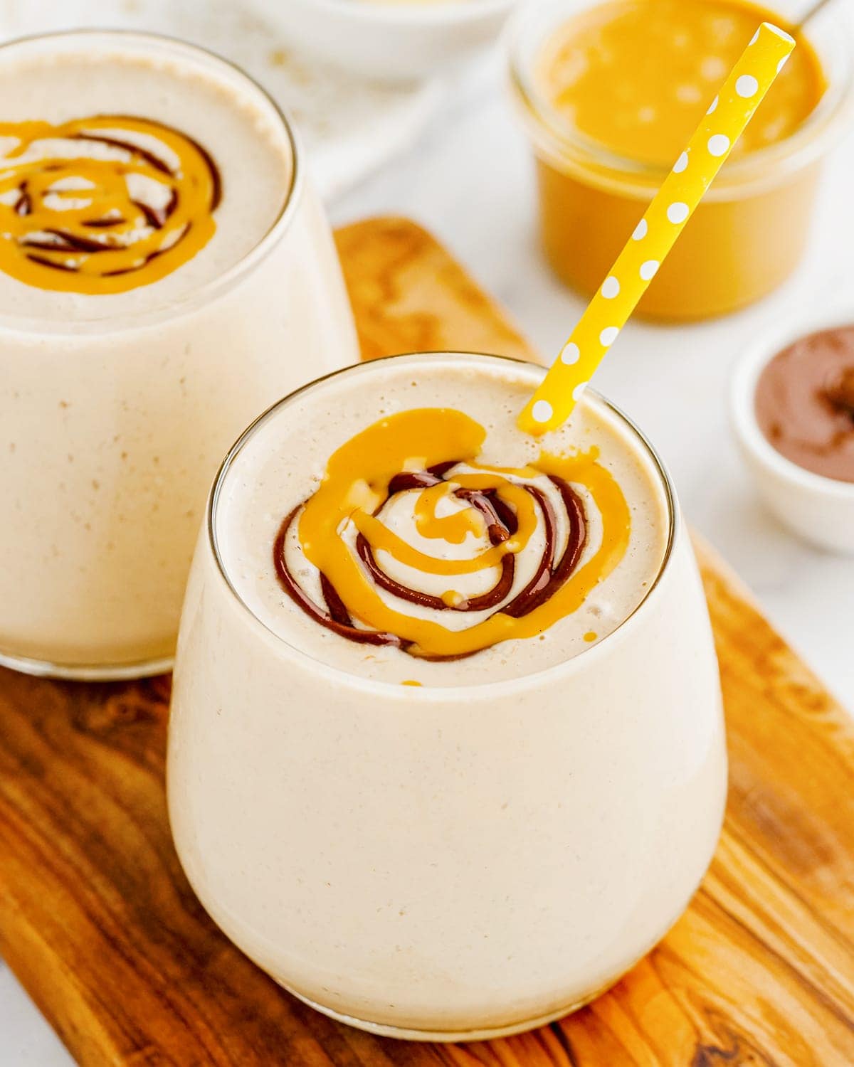 A glass of peanut butter banana smoothie on a wooden cutting board. The smoothie is topped with a swirl of peanut butter and chocolate syrup.