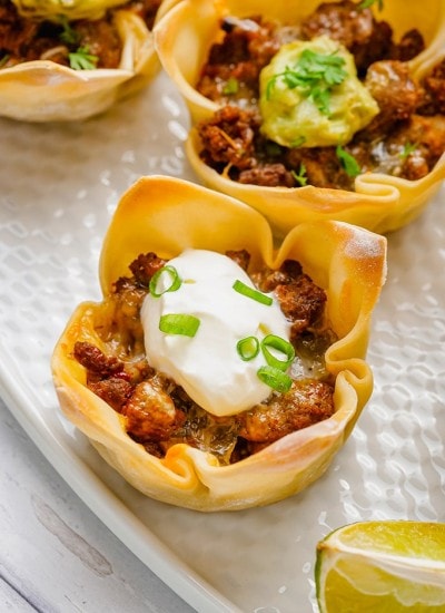 Close up photo of wonton taco cups with sour cream on top.