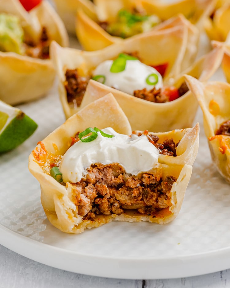 Close up photo of wonton taco cups with sour cream on top.