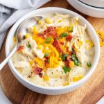 A bowl of chicken and potato chowder topped with shredded cheese, and bacon.