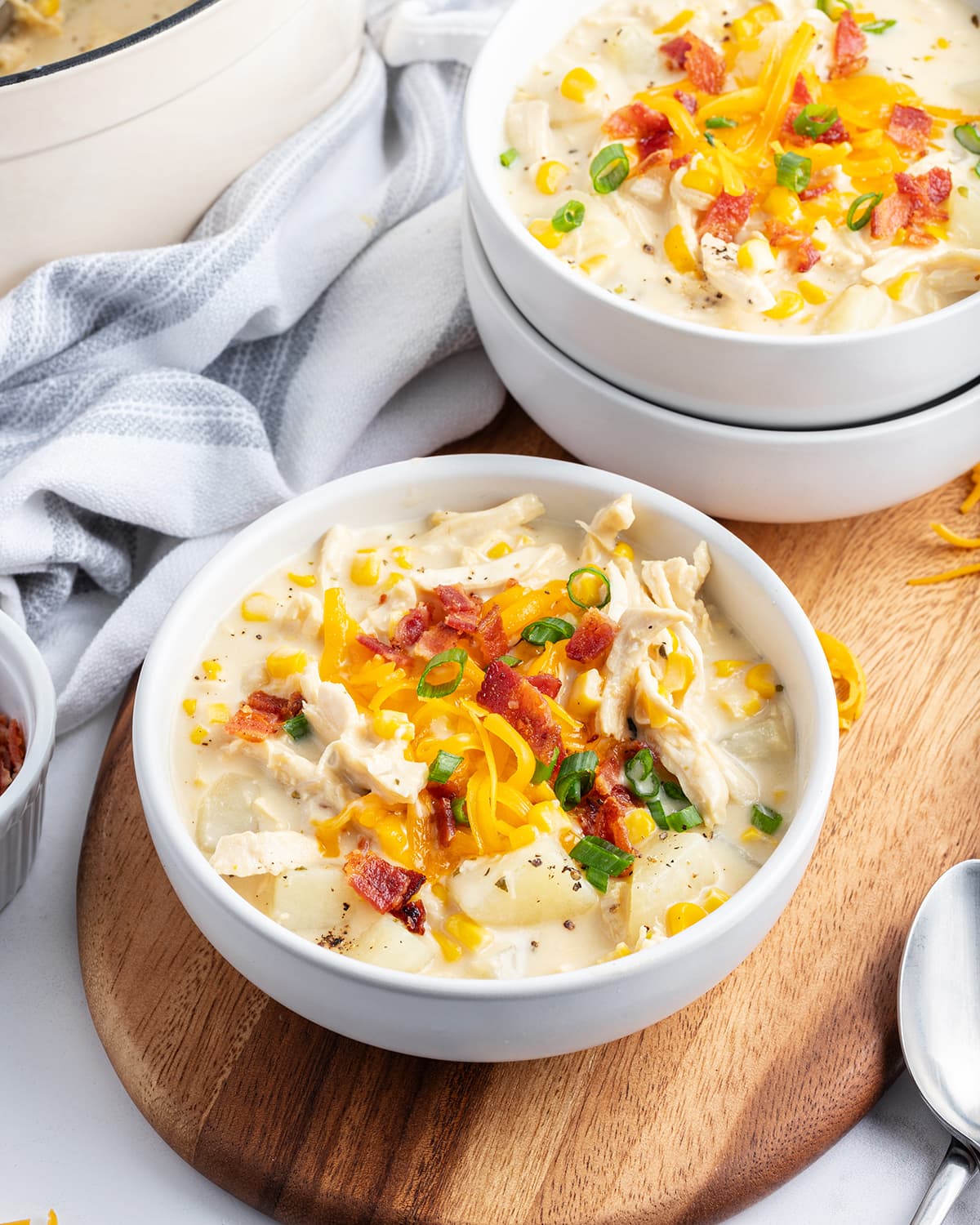 A bowl of cheese chicken chowder topped with bacon, green onions, and shredded cheese.
