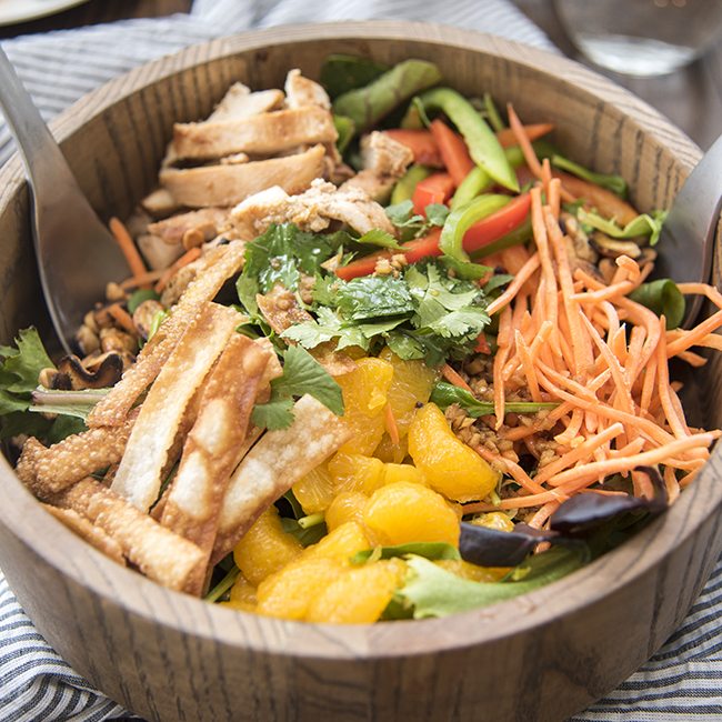 Angled image of oriental chicken salad in a wooden bowl.