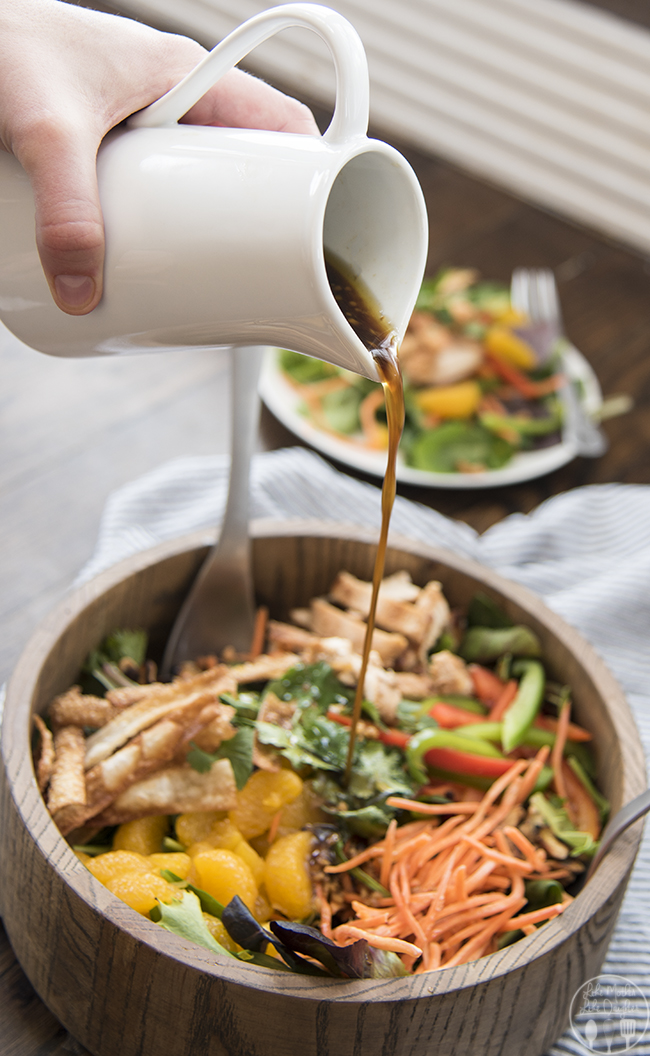 Angled image of oriental chicken salad in a wooden bowl with dressing being poured over it.