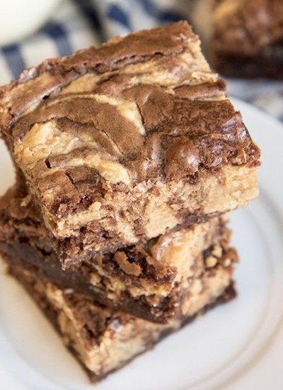 Above image of two peanut butter cheesecake brownies stacked on top of each other on a white plate.