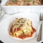 Angled image of spinach lasagna roll ups on a white plate with a fork.