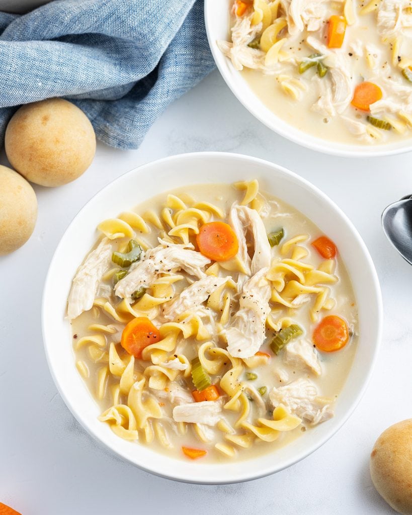 A bowl of creamy chicken noodle soup with shredded chicken, carrots, and wide egg noodles.