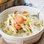 A bowl of creamy chicken noodle soup topped with carrots.