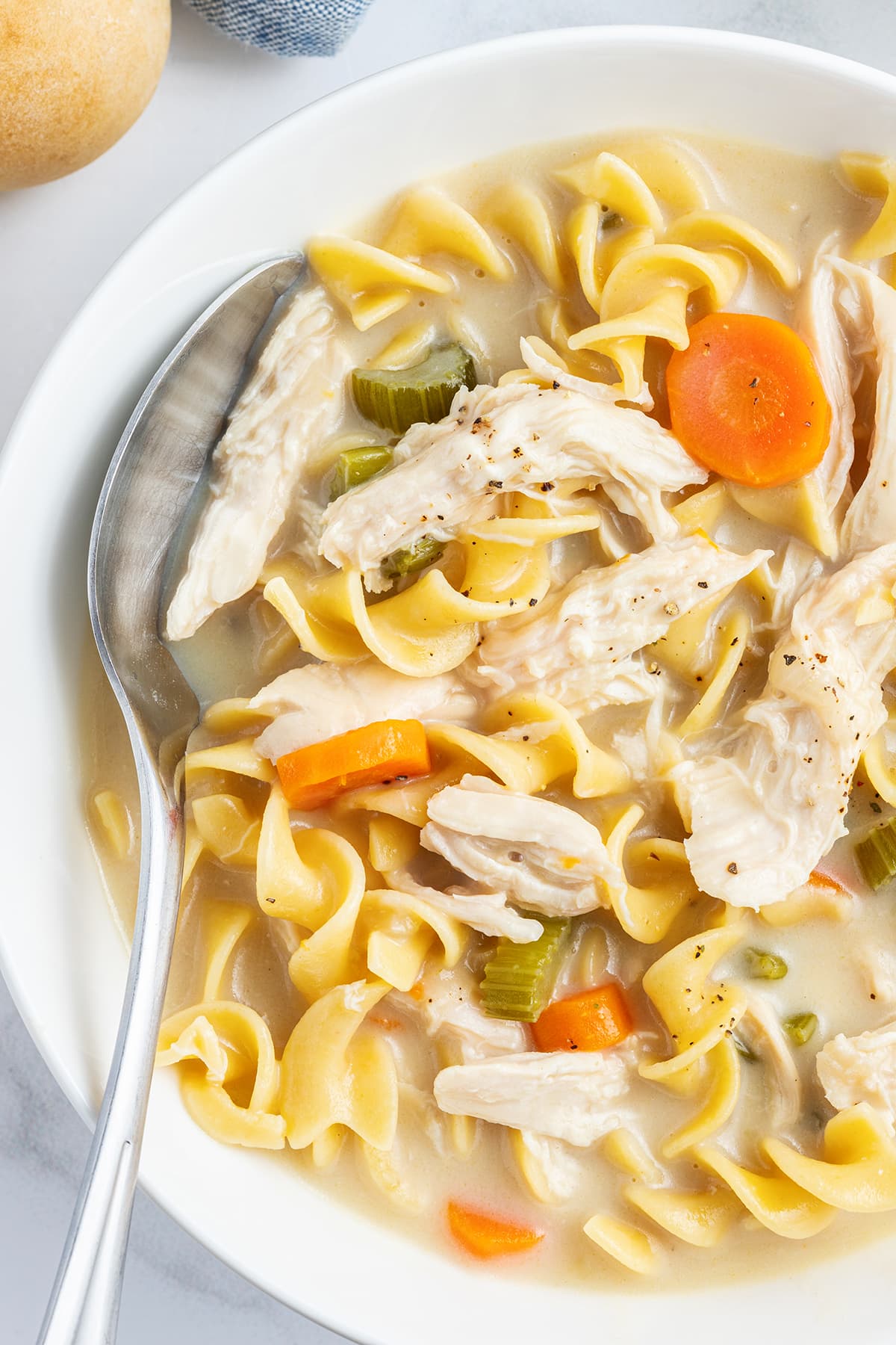 A close up of a bowl of chicken noodle soup with a spoon in it.