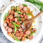 Above image of polska kielbasa stir fry in a white bowl with a wooden spoon.