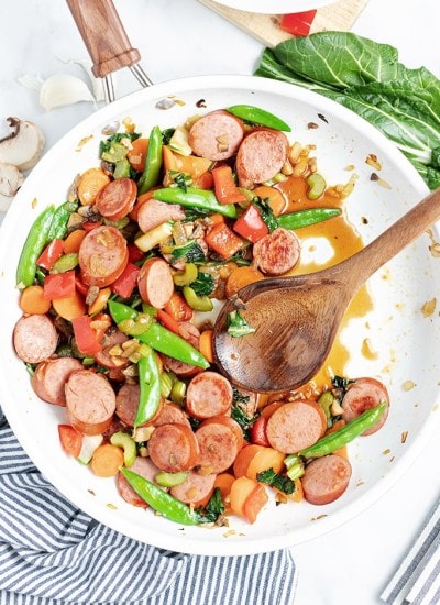 Above image of polska kielbasa stir fry in a white bowl with a wooden spoon.