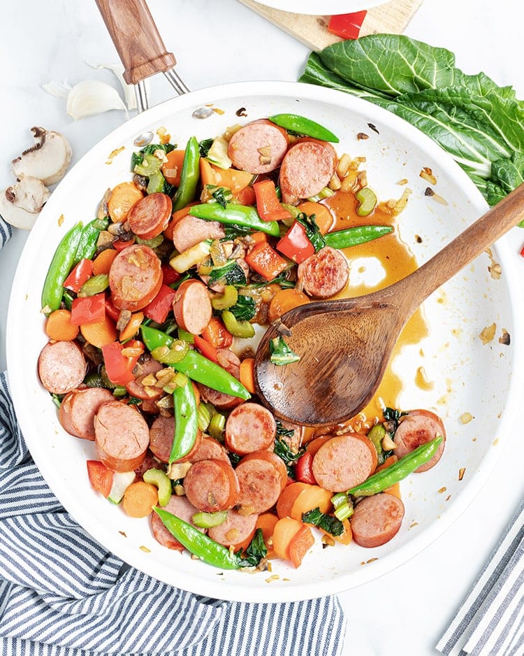 Above image of polska kielbasa stir fry in a white bowl with a wooden spoon.