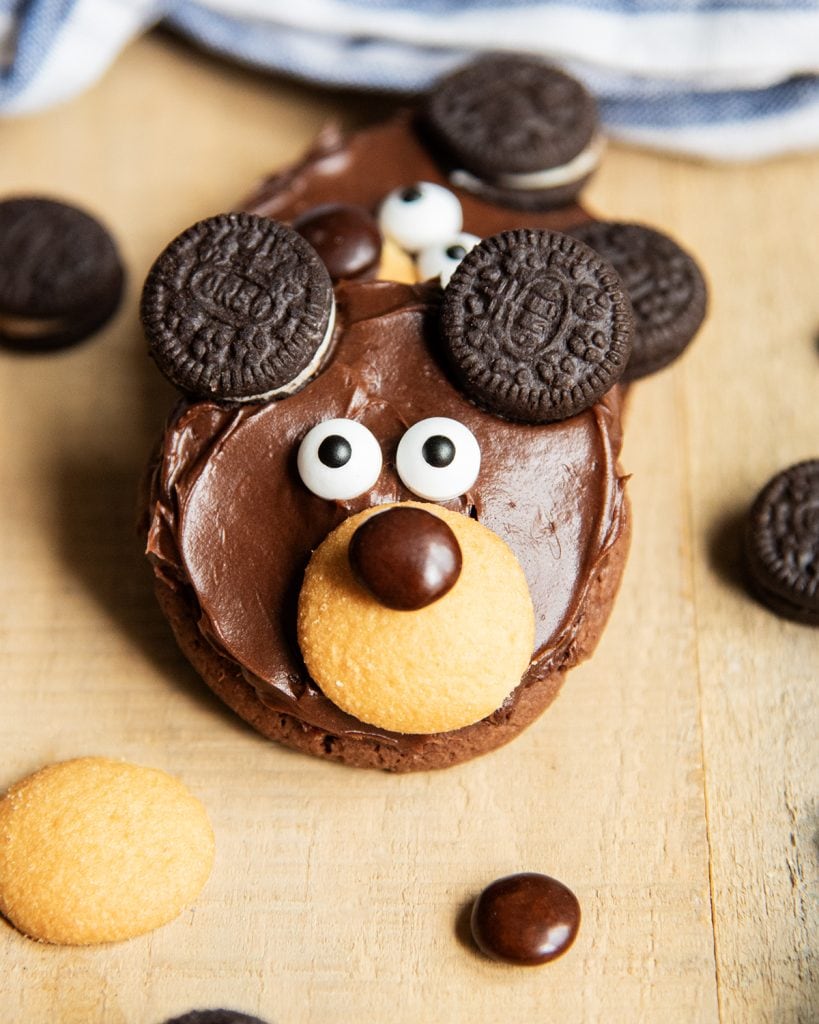 A bear Cookie decorated with chocolate frosting, and a cookie nose, candy eyes, and two Oreo eyes.