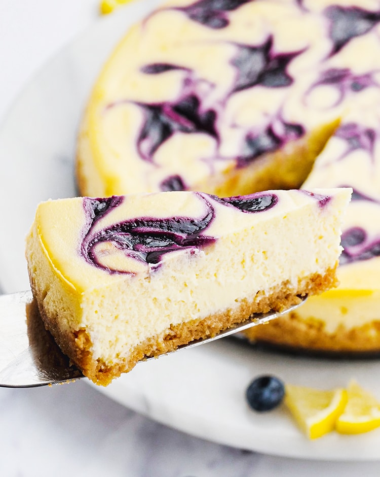 A slice of blueberry cheesecake being taken out of the whole cheesecake.