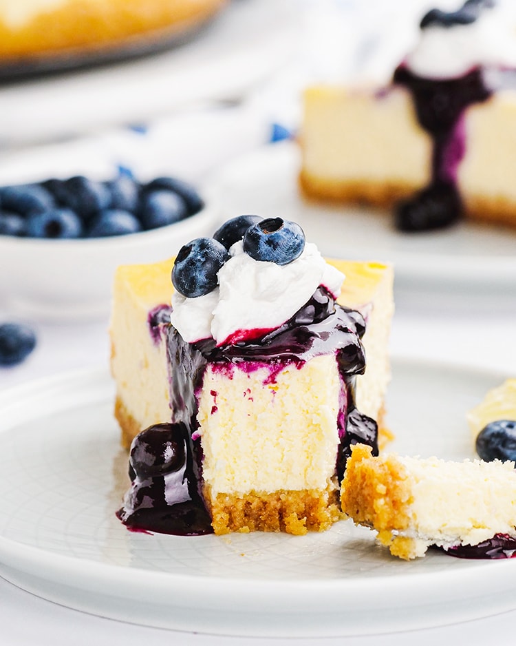 A slice of blueberry cheesecake with blueberry sauce and whipped cream on top with a fork bite taken out of the slice.