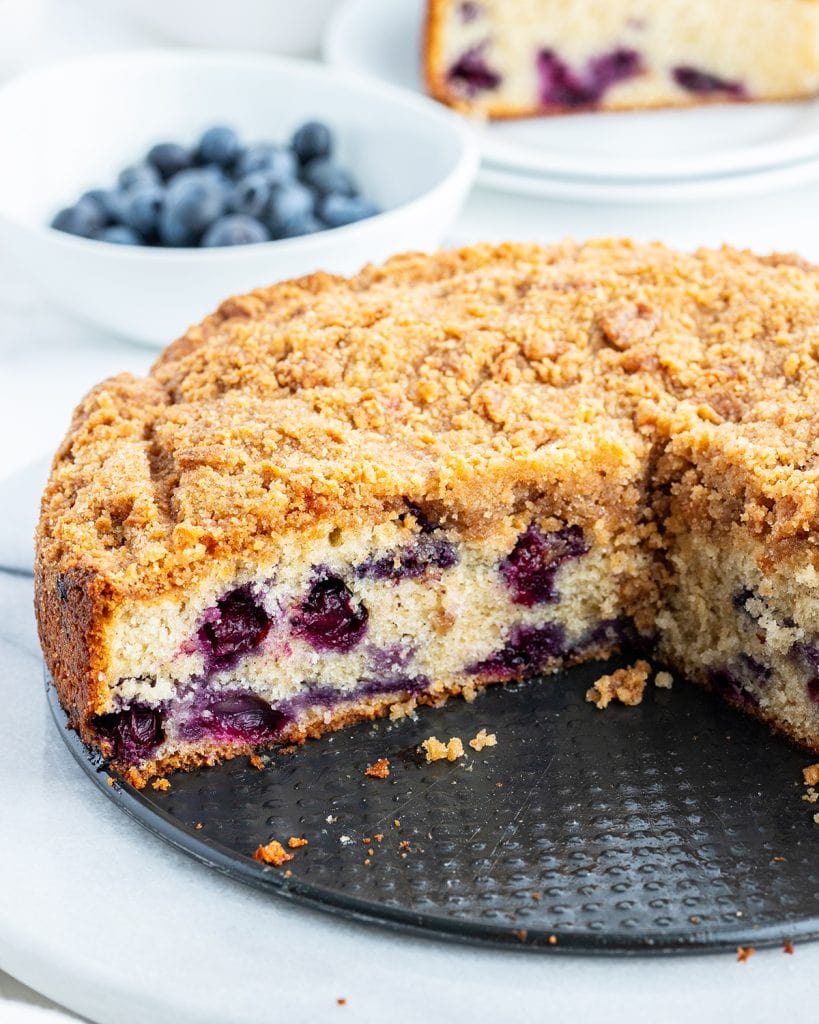 A coffee cake full of blueberries, on a springform pan, with slices removed so you can see the middle.