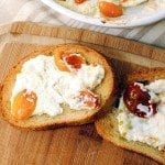 Above image of baked goat cheese spread on crispy bread on a wood platter.