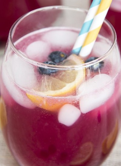 Close up image of a glass of blueberry lemonade with two straws.