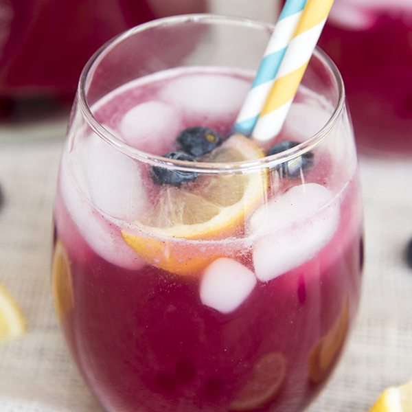 Close up image of a glass of blueberry lemonade with two straws.