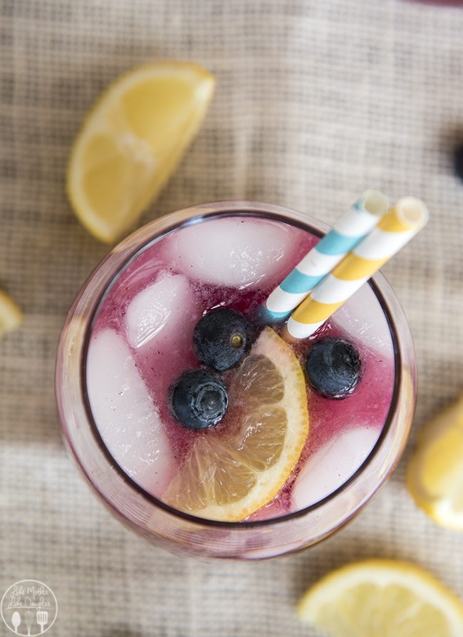 Above image of a glass of blueberry lemonade with two straws and lemon and blueberries on top.