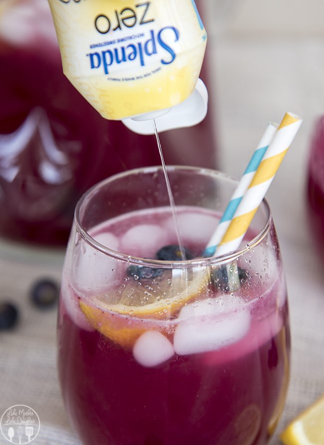 Side image of a glass of blueberry lemonade with two straws and liquid splenda being added.
