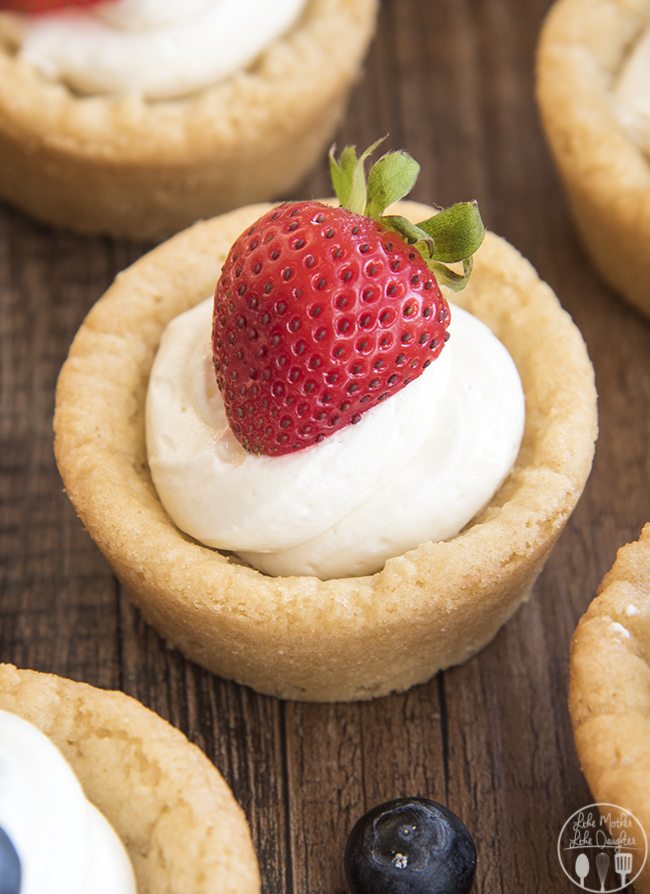 Sugar cookie cups filled with a swirl of white no bake cheesecake, topped with half of a strawberry.