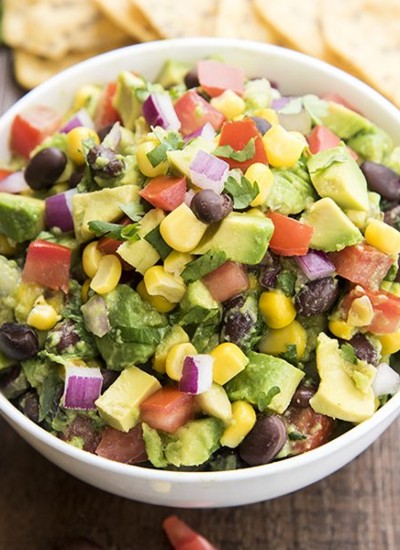 Above shot of a bowl of corn and black bean guacamole on a wood board.