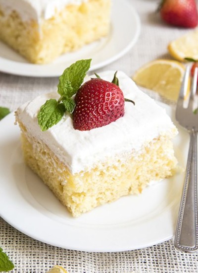 Side image of lemon poke cake with strawberry and mint on top on a white plate.