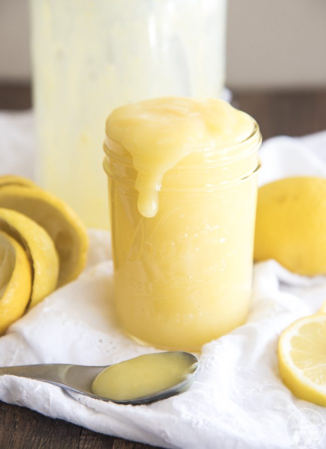 Angled image of lemon curd pouring over a mason jar with lemons surrounding it.