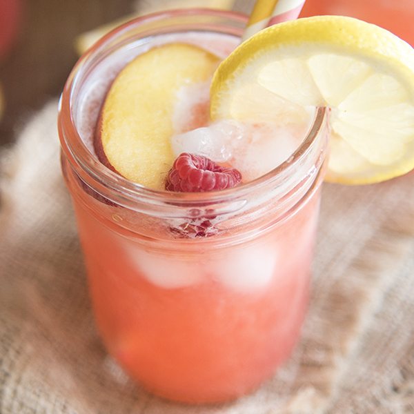 Above image of raspberry peach lemonade with peach, lemon, and raspberry on top.