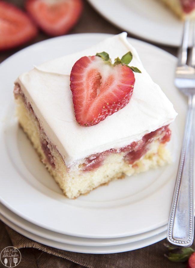 A slice of cake on a plate, with pokes full of strawberry sauce and topped with whipped cream and a slice of a strawberry.