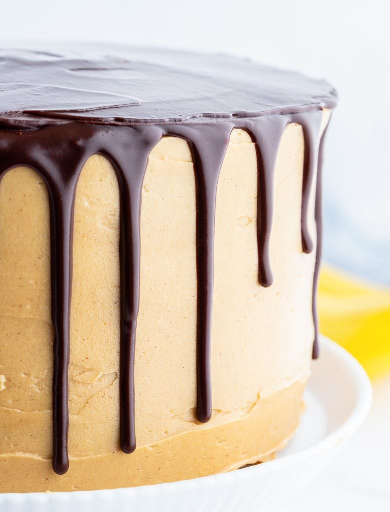 A side view of a triple layer cake covered in peanut butter frosting, and dripped with cocolate ganache.