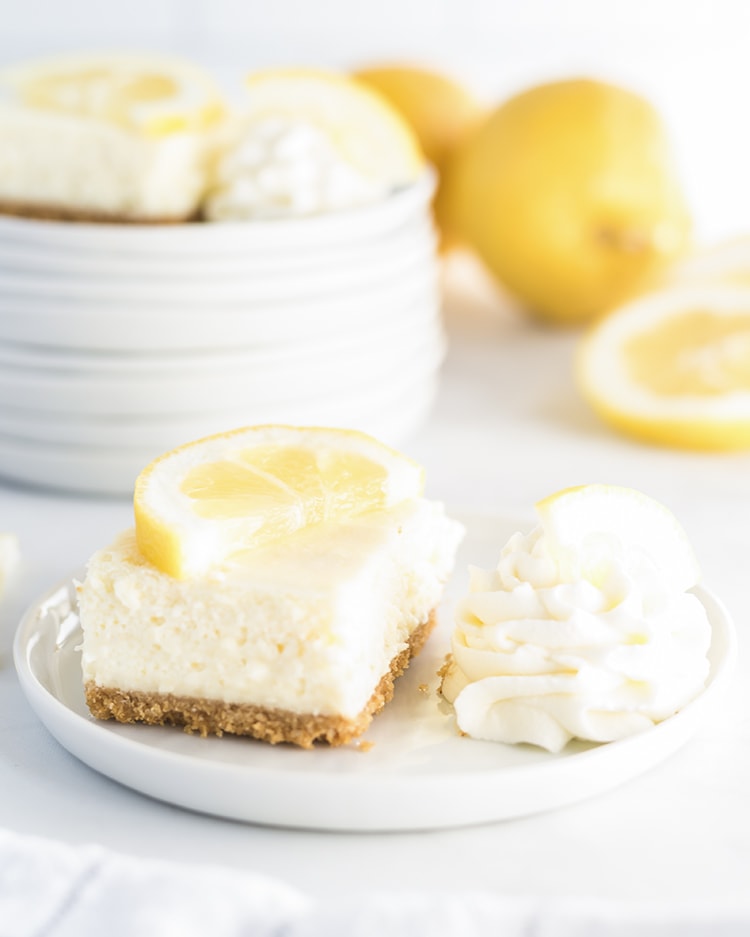 Lemon Cheesecake Bar on a white plate with whipped cream on the side.
