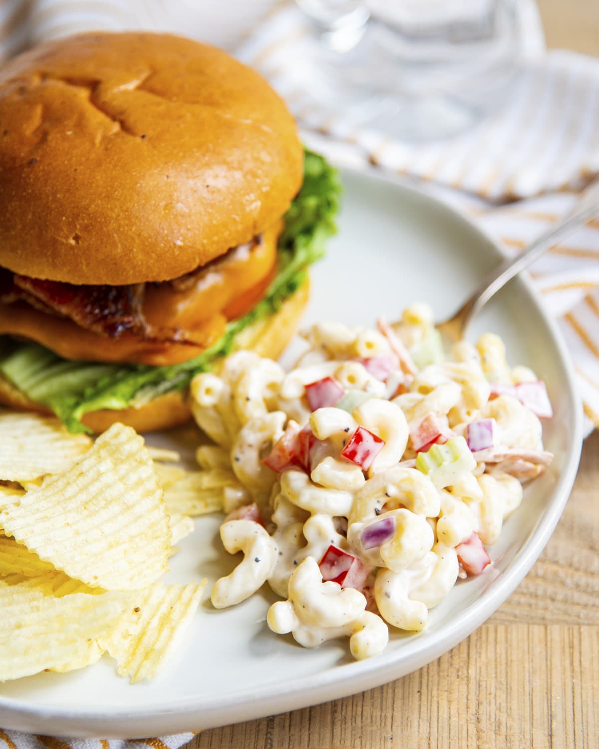 A plate of macaroni salad, chips, and a burger.