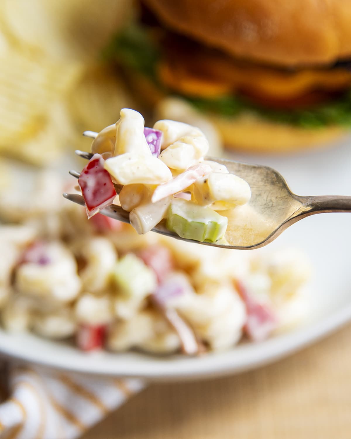 A forkful of macaroni salad with elbow noodles, celery, and red bell pepper.