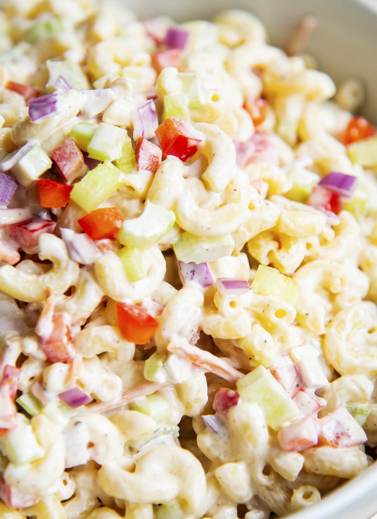 A close up of a bowl of macaroni salad with a creamy mayo dressing, and diced veggies like peppers, celery, and red onion.