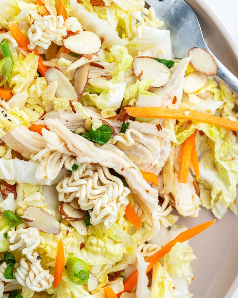 A close up of a plate of ramen noodle salad with cabbage, carrots, chicken, and green onions.