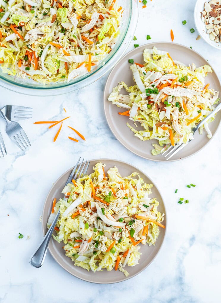 Two plates of ramen noodle salad with cabbage, carrots, chicken, and green onions.