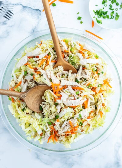 Cabbage and Ramen noodle salad tossed in a bowl with two wooden spoons.