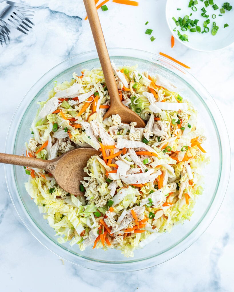 Cabbage and Ramen noodle salad tossed in a bowl with two wooden spoons.