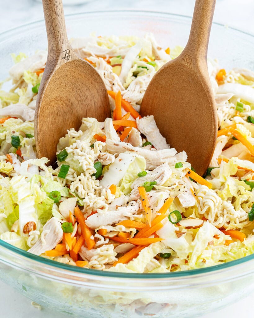Cabbage and Ramen noodle salad tossed in a bowl with two wooden spoons.