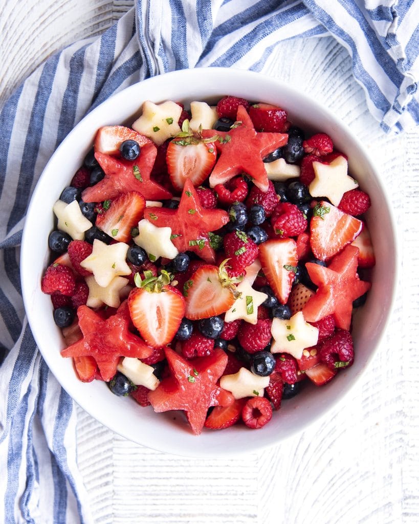An overhead photo of a bowl of a fourth of july fruit salad with watermelon, strawberries, blueberries, raspberries, and apple stars.